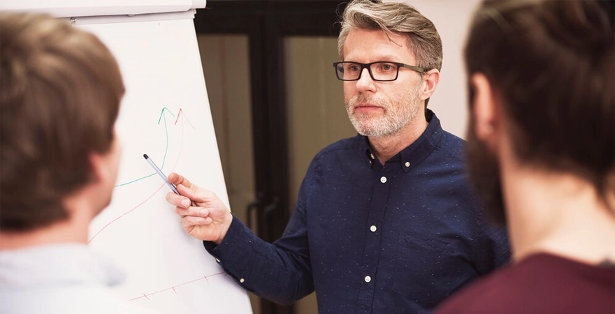 formateur pointant un feutre sur un tableau face à 2 apprenants